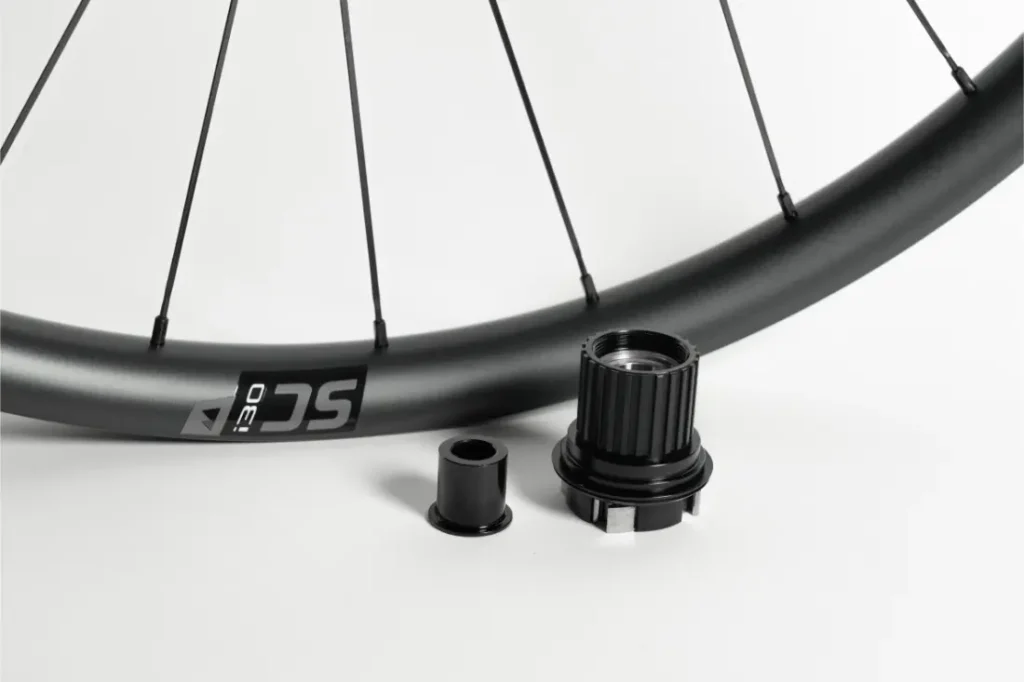 Se muestra una rueda de bicicleta con un primer plano del cuerpo del buje libre y dos adaptadores cilíndricos para el eje sobre un fondo blanco.