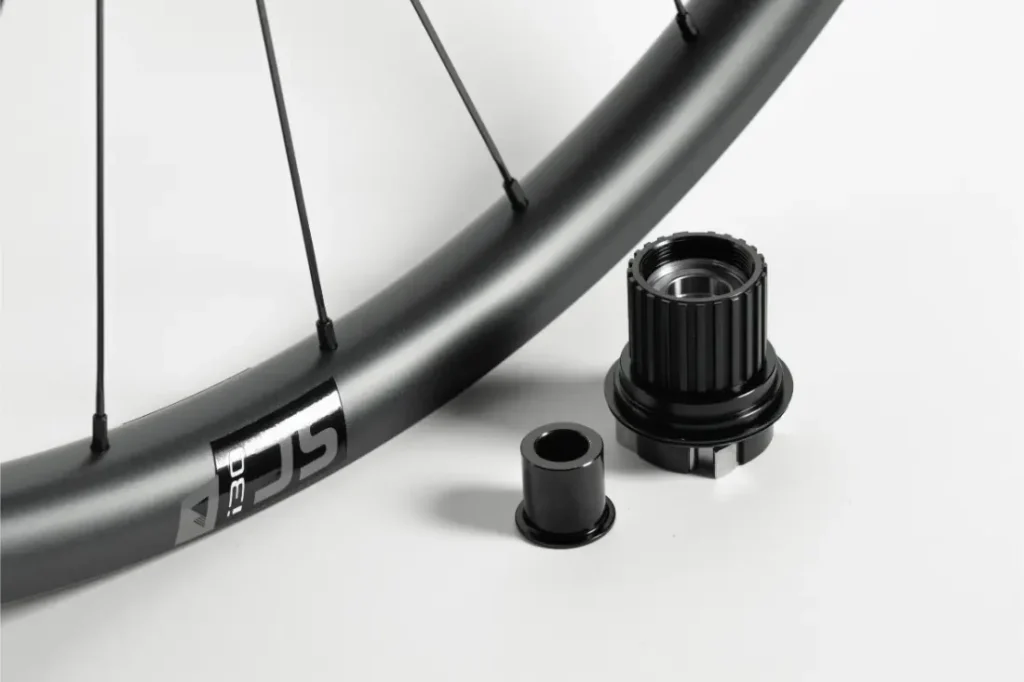 Un primer plano de la llanta de una bicicleta con radios, junto a dos componentes metálicos negros del buje, sobre un fondo blanco.