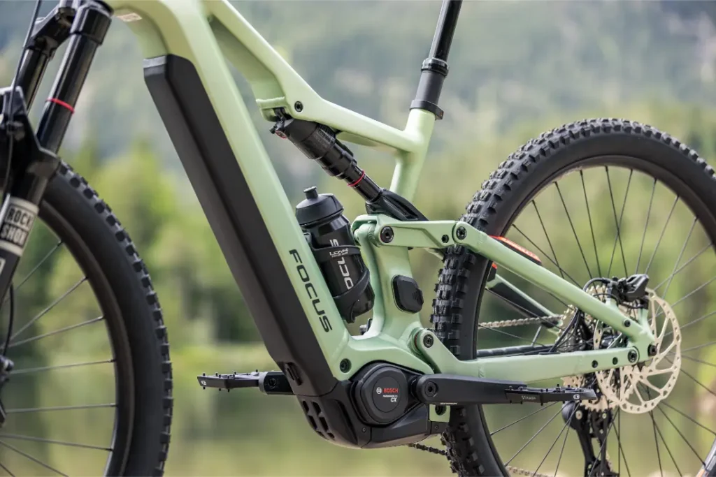 Primer plano de una bicicleta eléctrica de montaña Focus THRON de color verde, en el que se aprecian el cuadro, el motor Bosch, el bidón, la suspensión trasera y parte de la rueda trasera.