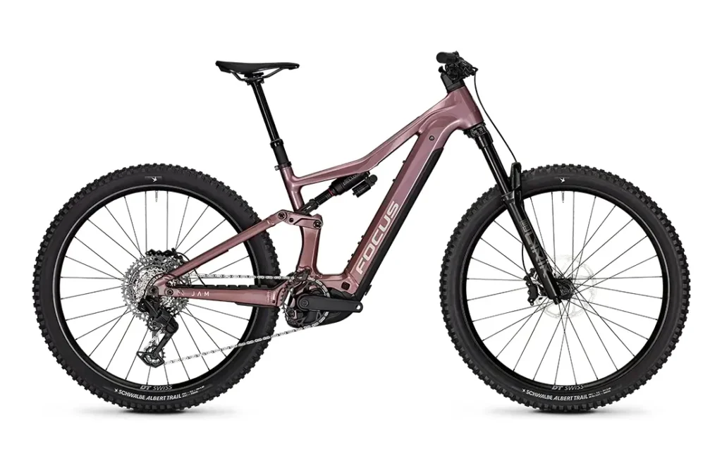 Una bicicleta de montaña de doble suspensión de la gama FOCUS e-MTB 2027, con cuadro rosa, ruedas negras, neumáticos anchos, frenos de disco y un motor central visible, fotografiada de perfil sobre un fondo blanco.
