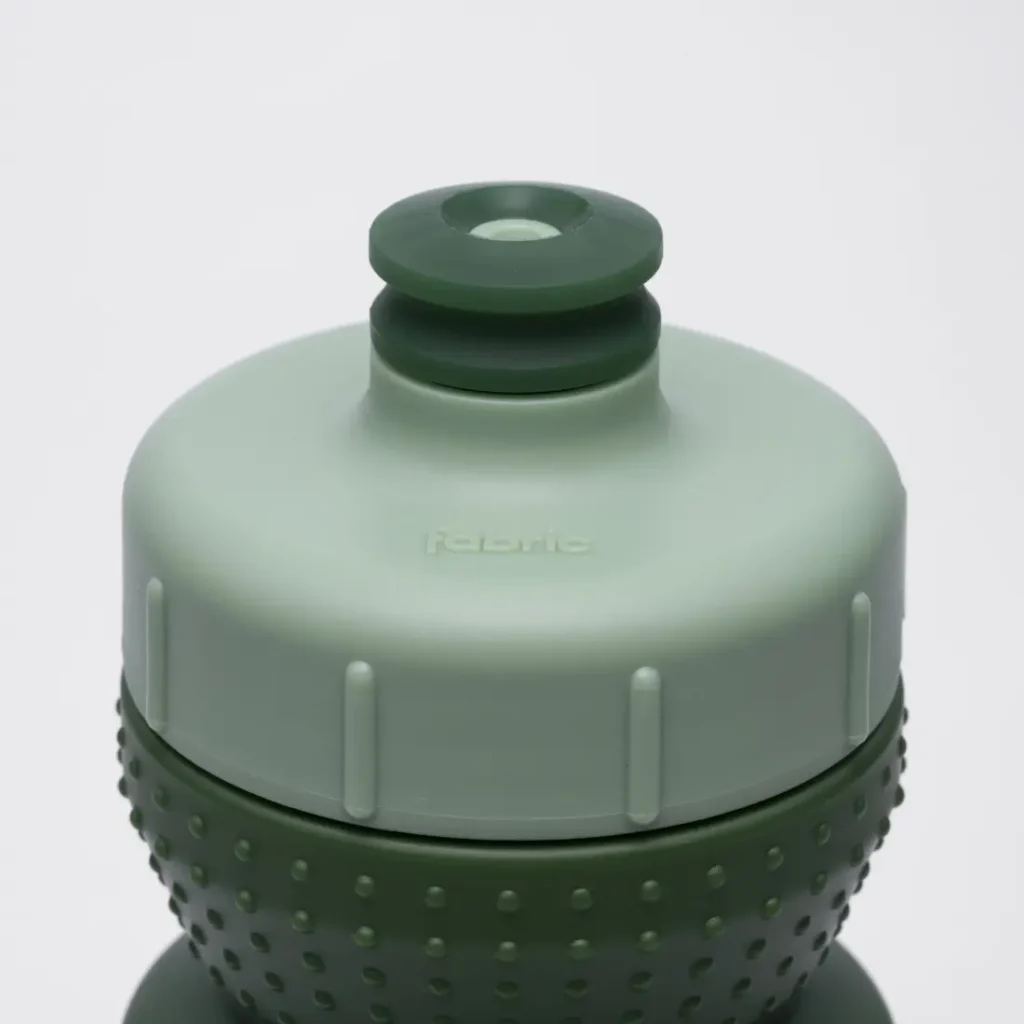 Primer plano de un tapón antimicrobiano «Fabric Gripper V2» de color verde y gris claro, con superficie texturizada para un mejor agarre y una boquilla circular de tipo «push-pull» en la parte superior, que ofrece protección permanente para la hidratación diaria.