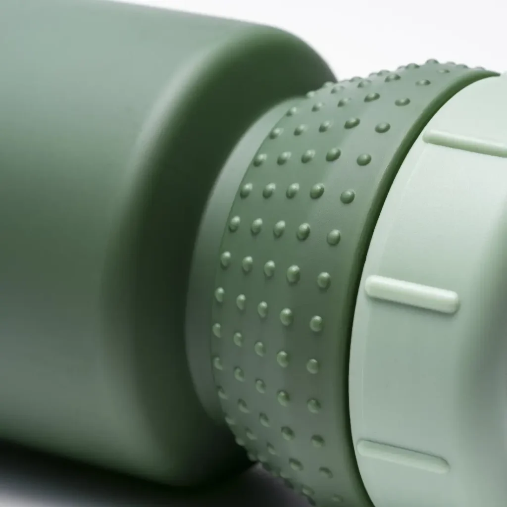 Primer plano de una tapa de botella de agua verde y con textura, con un agarre de goma y bordes estriados, en un bidón mate a juego que cuenta con protección antimicrobiana y el avanzado sistema Fabric Gripper V2 para un agarre seguro.