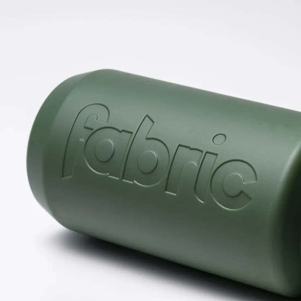 El bidón antimicrobiano Fabric Gripper V2, un objeto cilíndrico de color verde con la palabra «fabric» grabada en relieve en su superficie, ofrece protección permanente y aparece fotografiado sobre un fondo blanco liso.