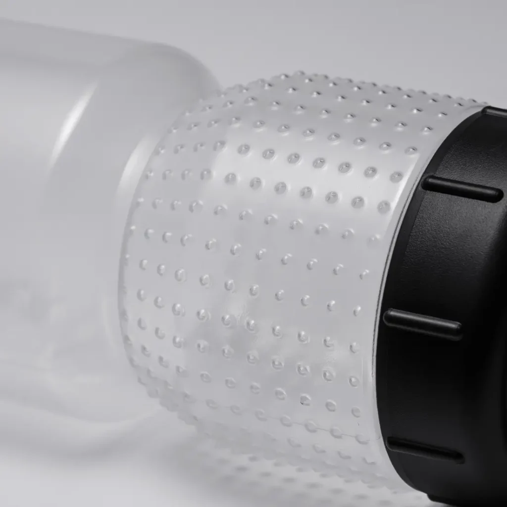 Primer plano de un bidón de plástico transparente con un agarre texturizado y punteado que incorpora la tecnología Fabric Gripper V2 y un tapón roscado negro, fotografiado sobre un fondo neutro. La botella está diseñada para ofrecer una mayor protección antimicrobiana y garantizar así una hidratación segura e higiénica.