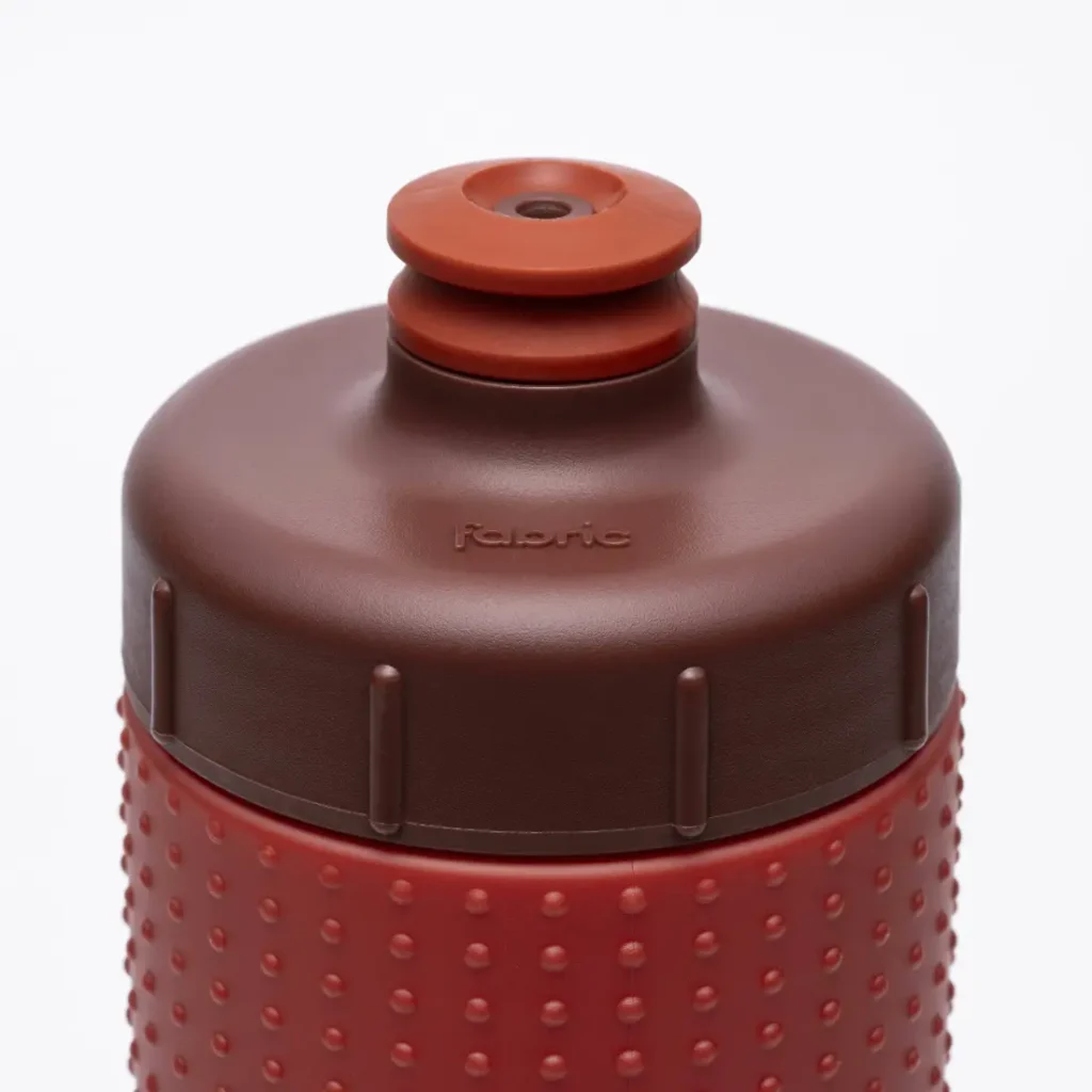 Primer plano de la parte superior de una botella de agua «Fabric Gripper V2» de color rojo y marrón, con un agarre texturizado y una boquilla de tipo «push-pull», que ofrece protección permanente gracias a su diseño antimicrobiano.