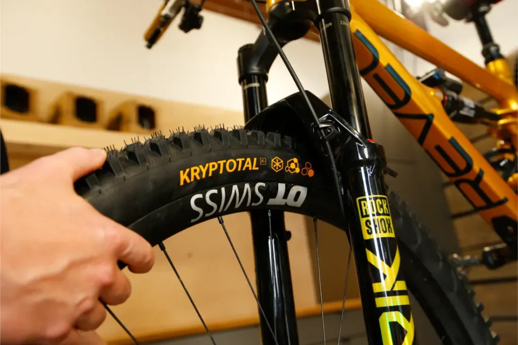 Una persona sostiene la rueda delantera de una bicicleta de montaña con las marcas «Kryptotal» y «DT Swiss», con especial atención a los neumáticos Continental para MTB y a la horquilla de suspensión Gravity.