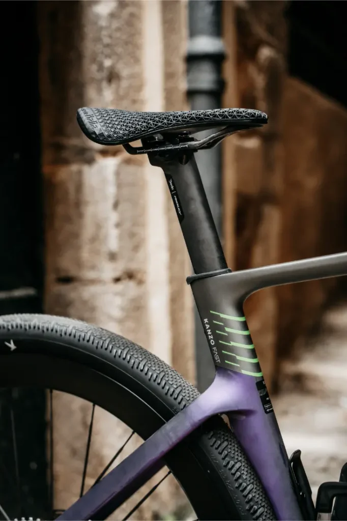 Primer plano del sillín, la tija del sillín y la rueda trasera de una bicicleta moderna Ridley Kanzo Fast 2.0, equipada con neumáticos aerodinámicos de 58 mm, con un muro de piedra como fondo.