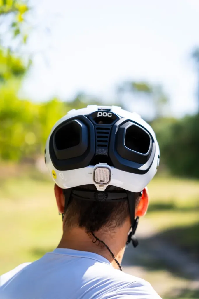 Una persona que lleva un casco de ciclismo POC blanco con dos grandes rejillas de ventilación negras, vista desde atrás, al aire libre en un día soleado. Perfecto para salidas por grava o carretera, este casco polivalente ofrece versatilidad y seguridad allá donde te lleve tu viaje.