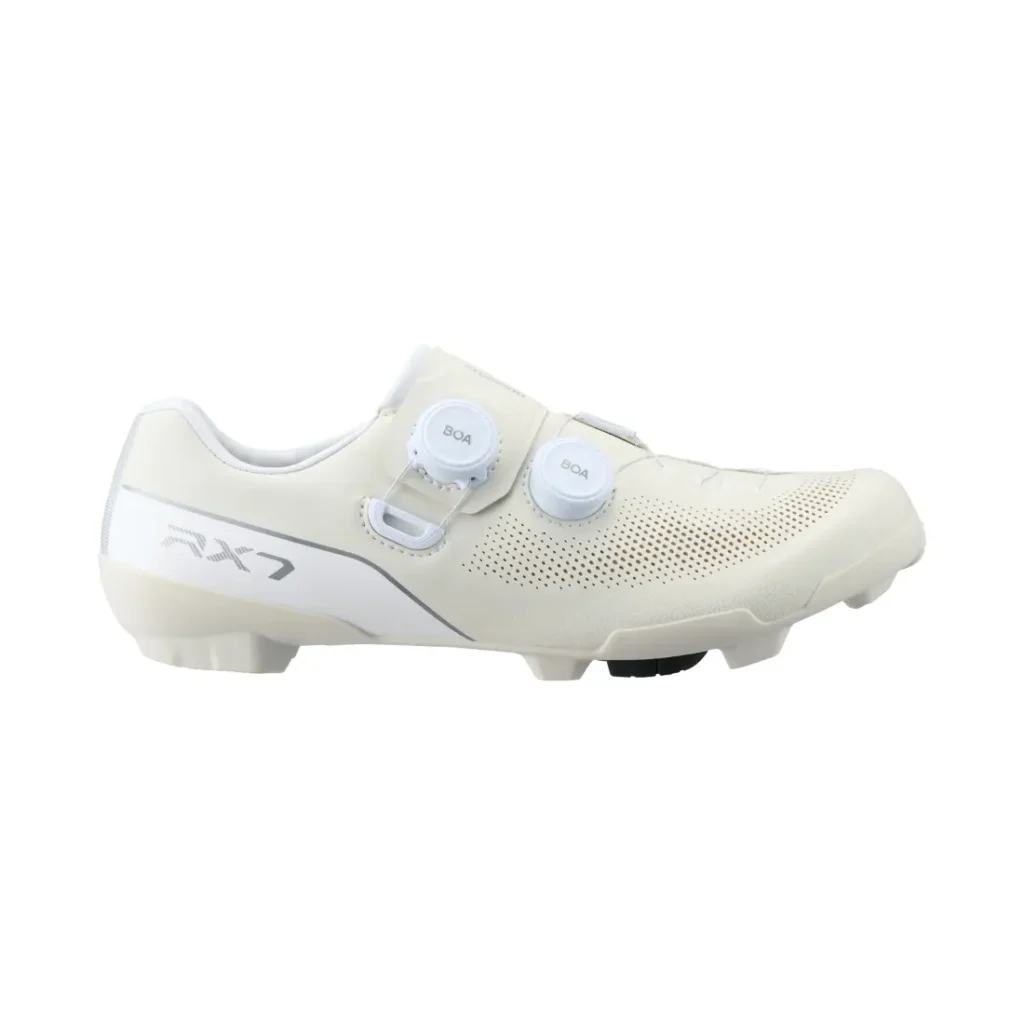 Vista lateral de unas zapatillas de ciclismo blancas Shimano RX710 con dos mandos BOA y detalles perforados, con la inscripción «RX7» cerca del talón, diseñadas con tecnología de competición para un rendimiento óptimo en grava.