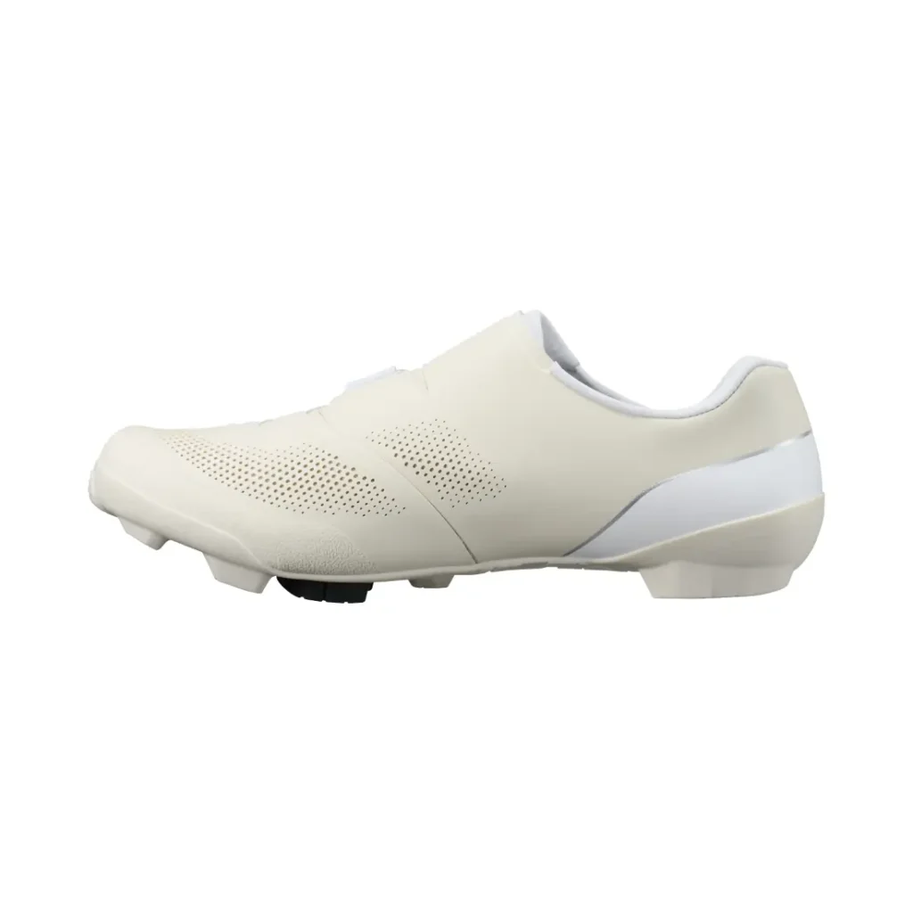 Vista lateral de una zapatilla de ciclismo blanca de perfil bajo, con parte superior perforada y suela moldeada, diseñada para pedales automáticos, que incorpora tecnología de competición ideal tanto para el ciclismo en carretera como en grava.