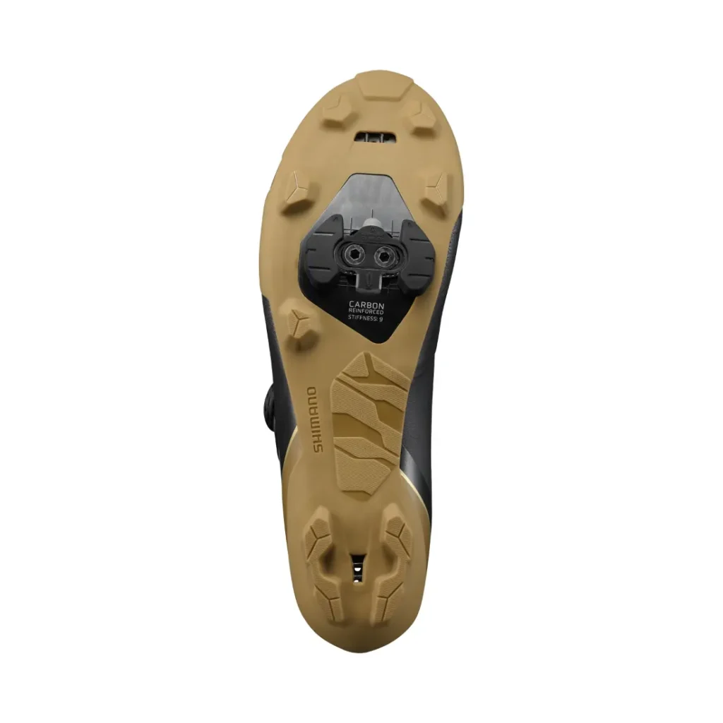 La parte inferior de unas zapatillas de ciclismo Shimano RX710 con suela de color beige, cala negra acoplada y dibujo de la suela visible. Las palabras «Shimano» y «Carbon» aparecen impresas en la suela, lo que destaca su tecnología de competición, ideal para rutas de grava.