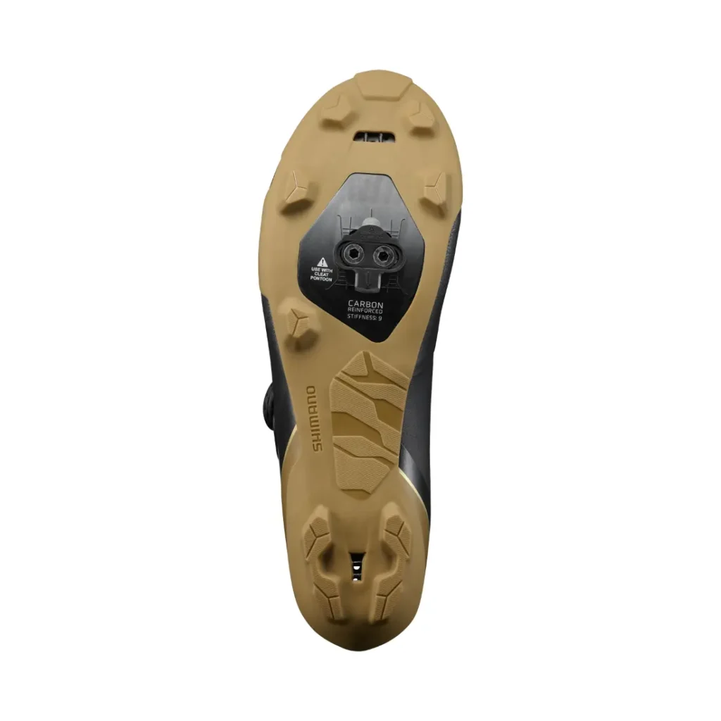 La imagen muestra la suela de color beige y negro de unas zapatillas de ciclismo Shimano RX710 con puntos de fijación para calas sobre un fondo blanco, lo que pone de relieve una tecnología de competición ideal para las zapatillas de gravel.