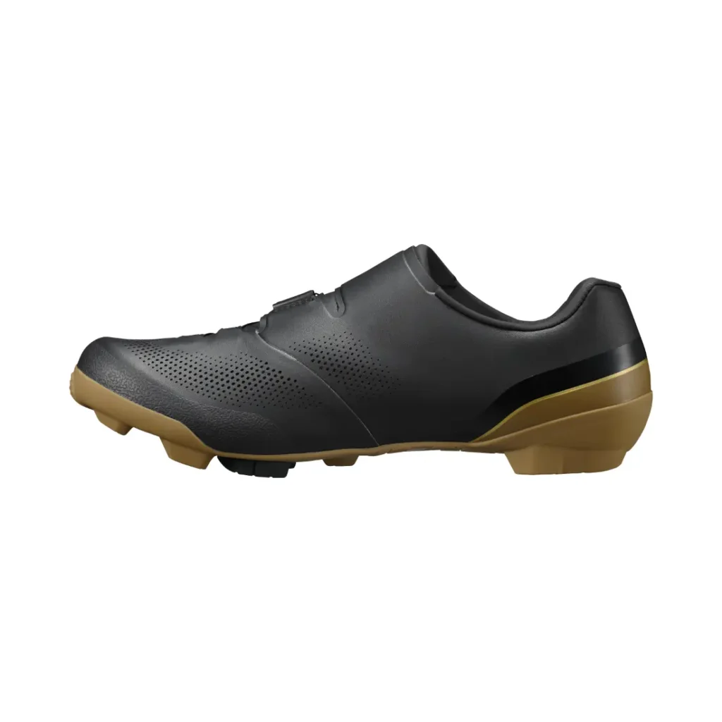 Zapatilla de ciclismo negra con parte superior perforada, cierre de velcro y suela marrón con dibujo, mostrada de perfil sobre un fondo blanco: ideal para salidas de gravel e inspirada en la tecnología de competición de las zapatillas Shimano.