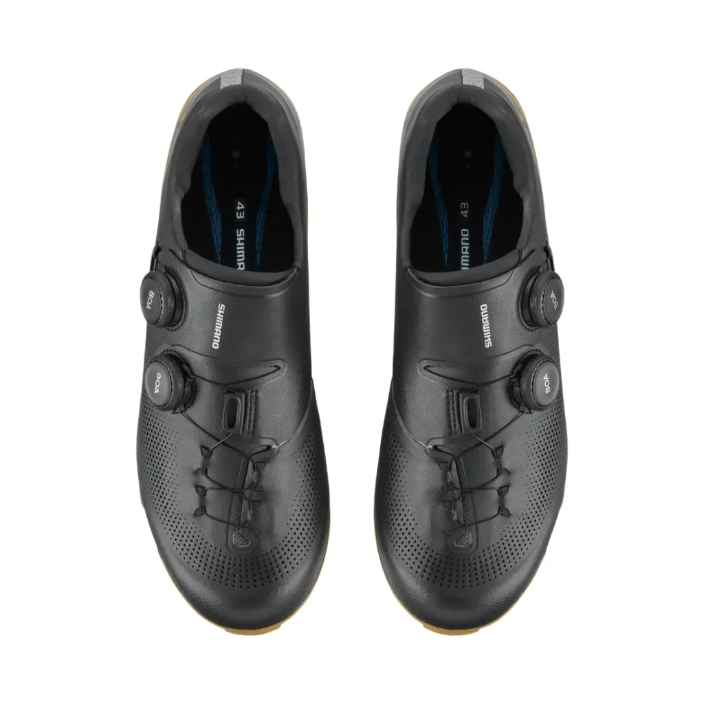 Un par de zapatillas de ciclismo Shimano negras con cierre de dial, diseñadas con tecnología de competición e ideales para salidas por grava, vistas desde arriba y expuestas sobre un fondo blanco.