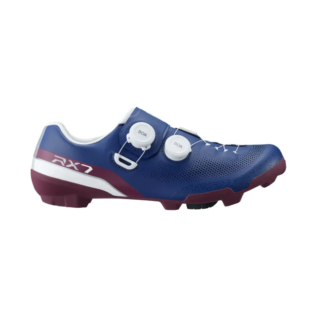 Unas zapatillas de ciclismo en azul y granate con detalles en blanco, dos cierres de rueda y el modelo «RX7» impreso en el lateral; las zapatillas Shimano RX710 combinan tecnología de competición ideal para el gravel.