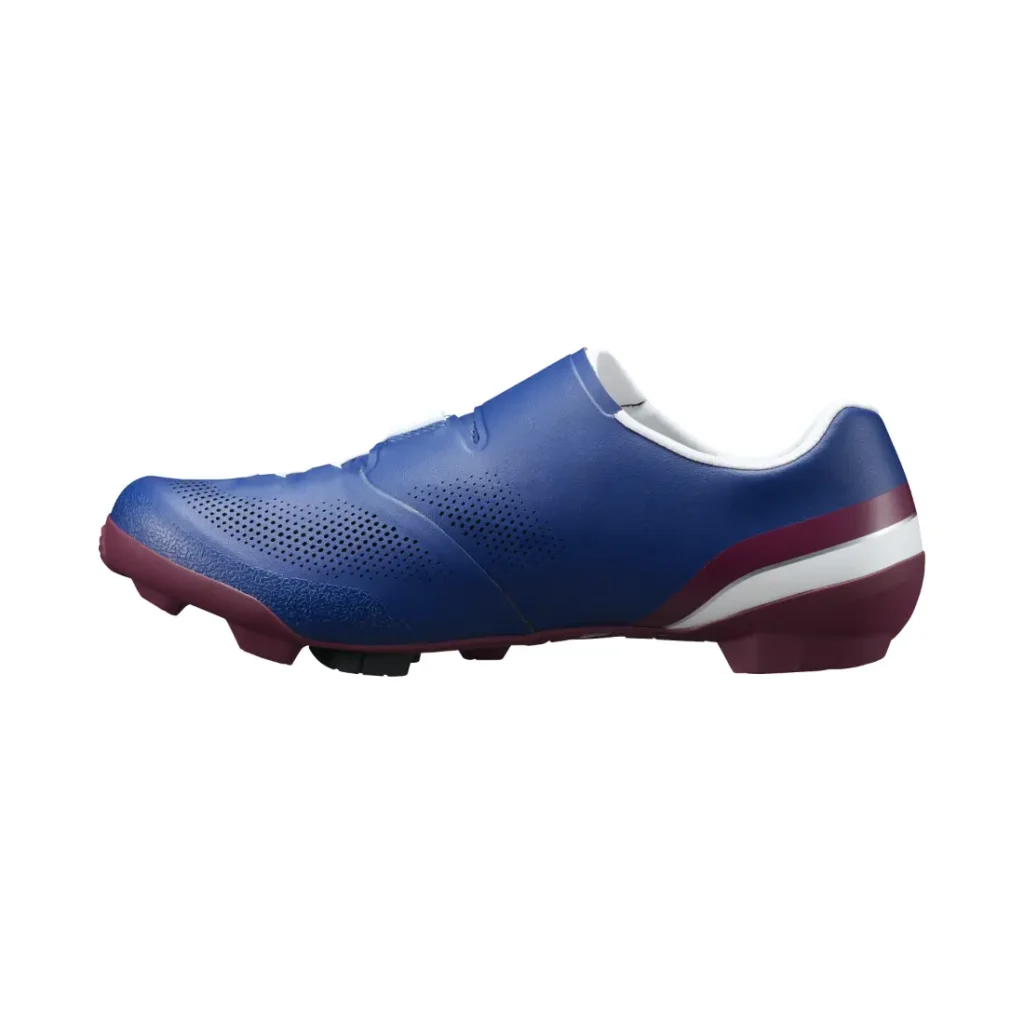 Vista lateral de unas zapatillas de ciclismo Shimano RX710 azules con detalles en granate y perforaciones, que incorporan tecnología de competición para un rendimiento óptimo sobre grava, mostradas sobre un fondo blanco.