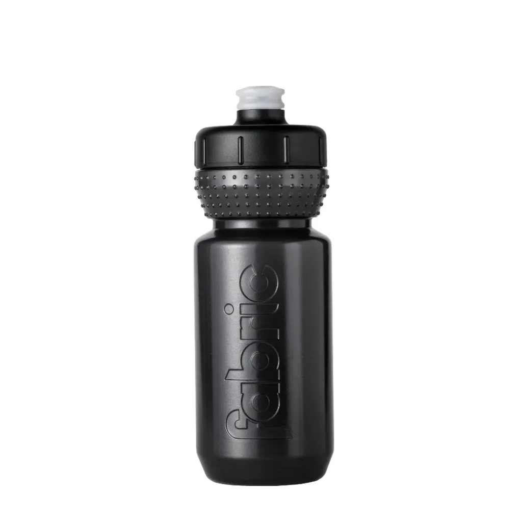Botella deportiva de plástico negro con agarre texturizado y boquilla de tipo «push-pull». La palabra «fabric» aparece grabada en relieve verticalmente en el lateral, lo que destaca su identidad como Fabric Gripper V2. La botella se presenta en posición vertical sobre un fondo blanco, ofreciendo tanto estilo como protección antimicrobiana para tus necesidades de hidratación.