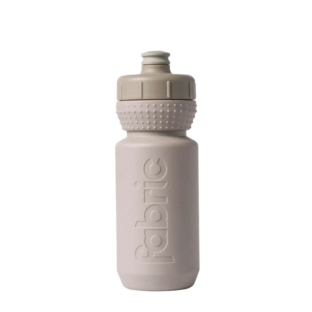 Botella de agua de plástico de color beige con un agarre texturizado y un tapón de tipo «push-pull», con la palabra «fabric» grabada en relieve en vertical en el lateral. Este bidón antimicrobiano Fabric Gripper V2 ofrece protección permanente para tus necesidades de hidratación.