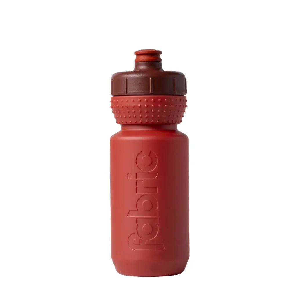 Botella de plástico rojo «Fabric Gripper V2» con agarre texturizado y el logotipo «fabric», que cuenta con una tapa marrón de rosca y una boquilla de tipo «push-pull», representada en posición vertical sobre un fondo blanco. Esta botella antimicrobiana ofrece protección permanente para tus necesidades de hidratación.