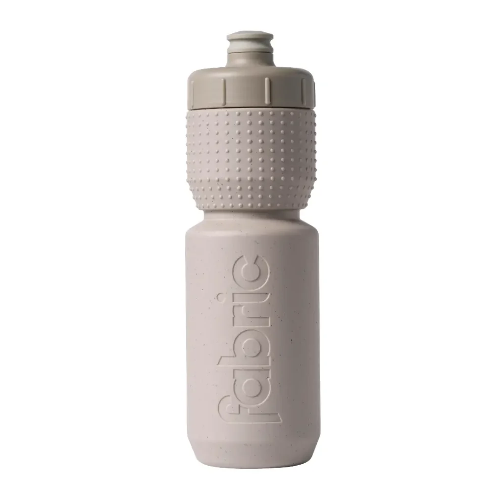 Botella de agua de plástico de color beige con un agarre texturizado y un tapón de rosca, en cuyo lateral aparece la palabra «fabric» grabada en relieve en vertical. La Fabric Gripper V2 ofrece protección permanente como botella antimicrobiana, lo que garantiza que tu bebida se mantenga fresca y limpia.