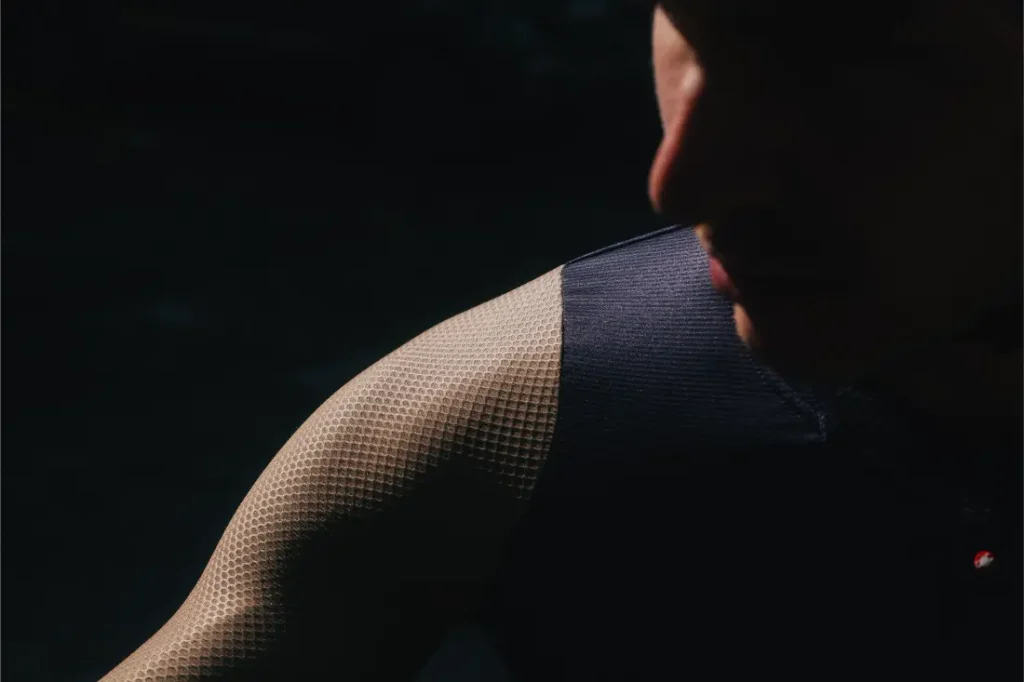 Primer plano de una persona con un top sin mangas y con textura, con una iluminación espectacular que resalta su hombro y su brazo sobre un fondo oscuro, creando un contraste llamativo que recuerda al estilo de las campañas de Castelli Transition.