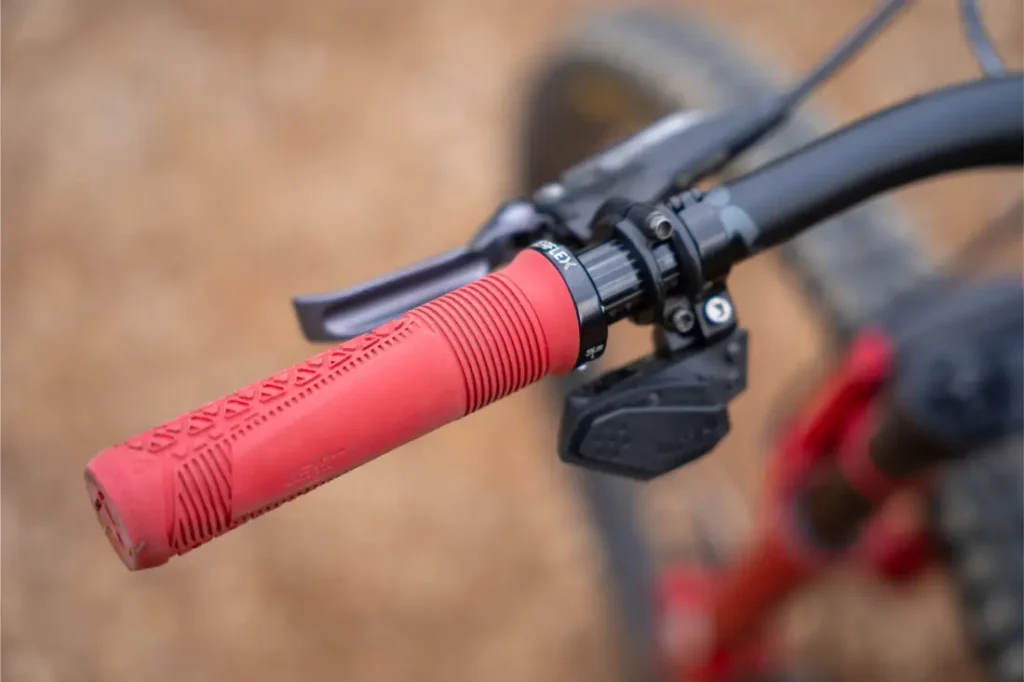 Primer plano de un puño rojo ReaFlex 6.0 en el manillar de una bicicleta, en el que se aprecian la palanca de freno, la palanca de cambios y parte del manillar negro Leatt Launch Control 6.0.
