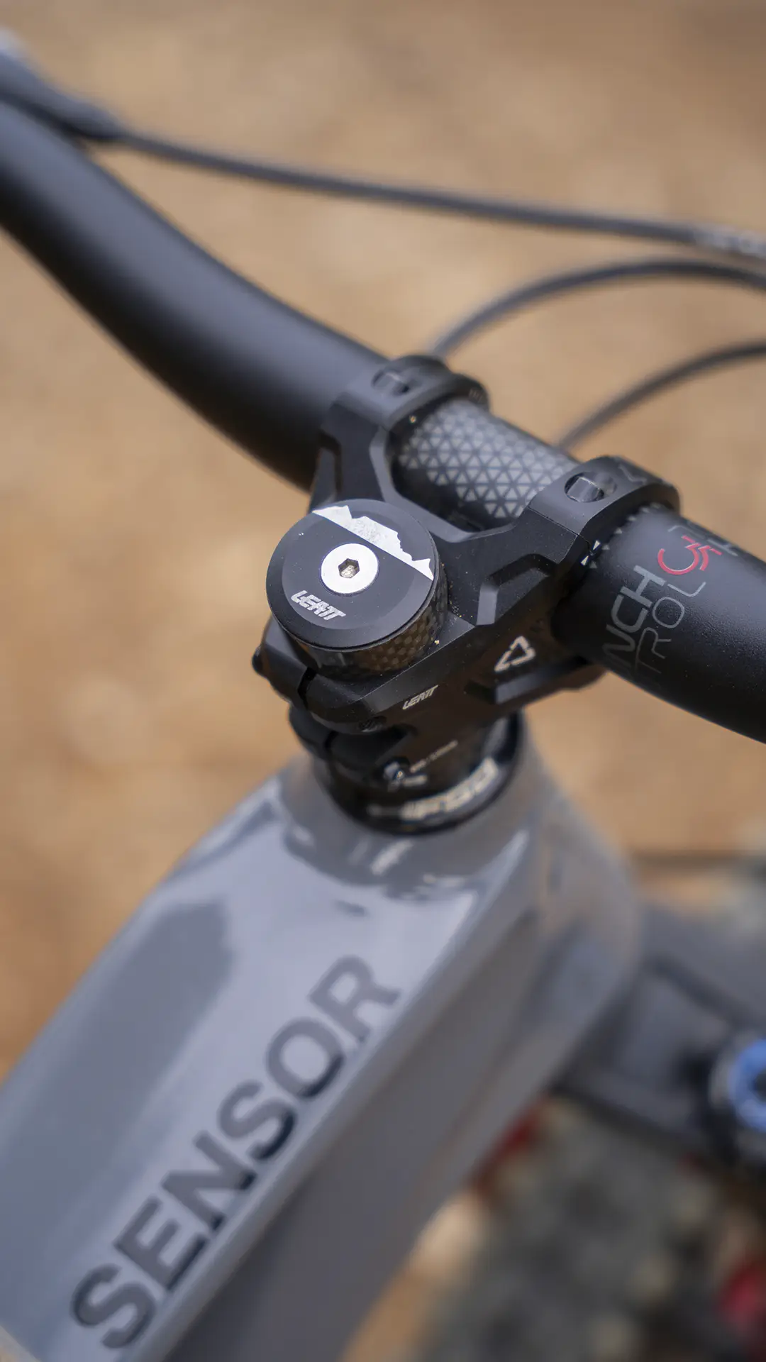 Primer plano del manillar y la potencia de una bicicleta, en el que se aprecia la marca «SENSOR» en el cuadro; se muestra el manillar Leatt Launch Control 6.0, así como la tapa superior y parte del cable de freno.