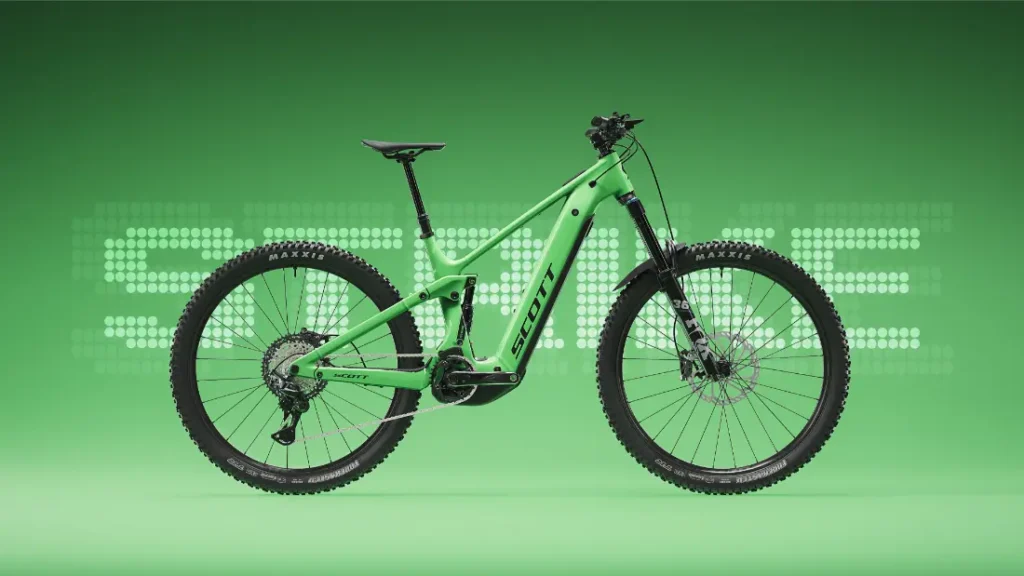 Una bicicleta de montaña eléctrica de doble suspensión SCOTT Strike 2027 de color verde, equipada con un potente motor Bosch CX, aparece en una vista de perfil sobre un fondo verde, con la palabra «SMILE» escrita en letras punteadas detrás de ella, lo que destaca tanto su rendimiento como su comodidad.