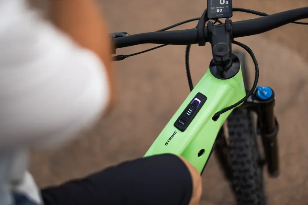 Primer plano de una persona sentada en una bicicleta eléctrica SCOTT Strike 2027 de color verde, en el que se aprecian el indicador de batería y el manillar ergonómico de la bicicleta, junto con parte de la rueda delantera y el potente motor Bosch CX.