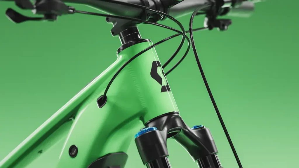 Primer plano de la parte delantera del cuadro de una bicicleta SCOTT Strike 2027 de color verde, en el que se aprecian la horquilla de suspensión, los cables y el logotipo negro, sobre un fondo verde liso. Diseñado para ofrecer un confort óptimo, este modelo cuenta con opciones de integración avanzadas, como el motor Bosch CX.