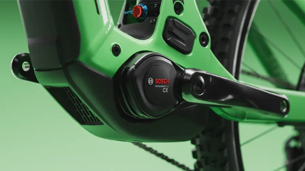Primer plano de un motor Bosch Performance CX instalado en una bicicleta eléctrica SCOTT Strike 2027 de color verde, en el que se aprecian la biela, la carcasa del motor y parte de la rueda trasera sobre un fondo verde, lo que resalta a la perfección tanto la avanzada tecnología del motor Bosch CX como el mayor confort para el ciclista.