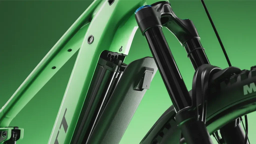 Primer plano de una bicicleta de montaña eléctrica SCOTT Strike 2027 de color verde en el que se aprecian el compartimento de la batería y la suspensión delantera sobre un fondo verde, destacando su comodidad y su potente motor Bosch CX.