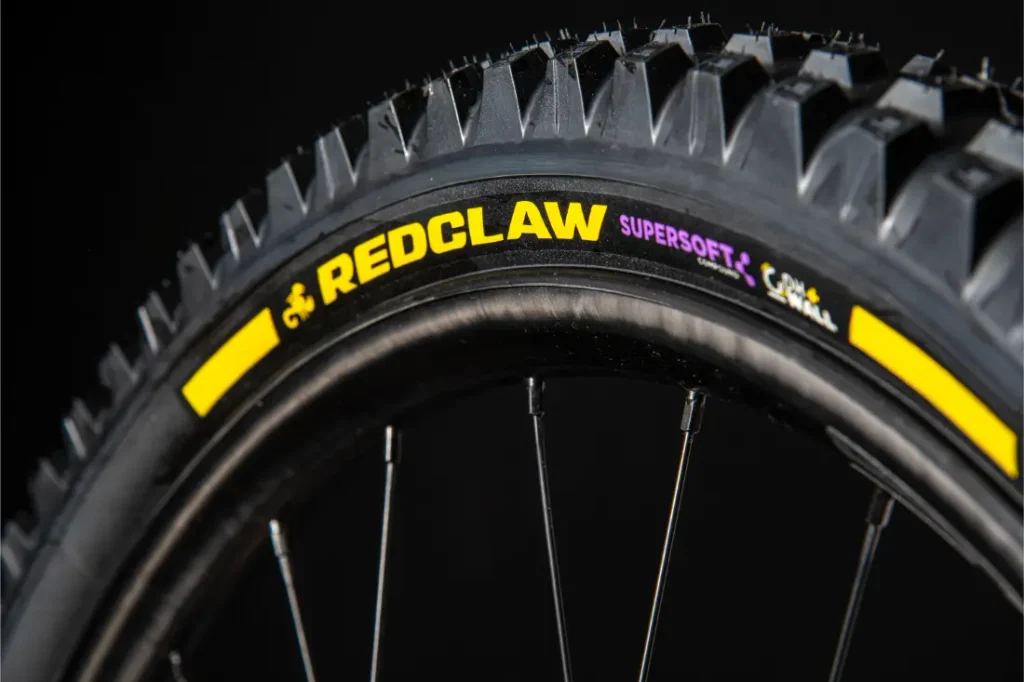 Primer plano de una rueda de bicicleta en el que se aprecia la banda de rodadura y la inscripción «REDCLAW SUPERSOFT» en el flanco negro con detalles en amarillo, sobre un fondo oscuro: ideal para ciclistas que buscan neumáticos de MTB de alto rendimiento inspirados en tecnologías presentes en modelos como el Pirelli Scorpion.