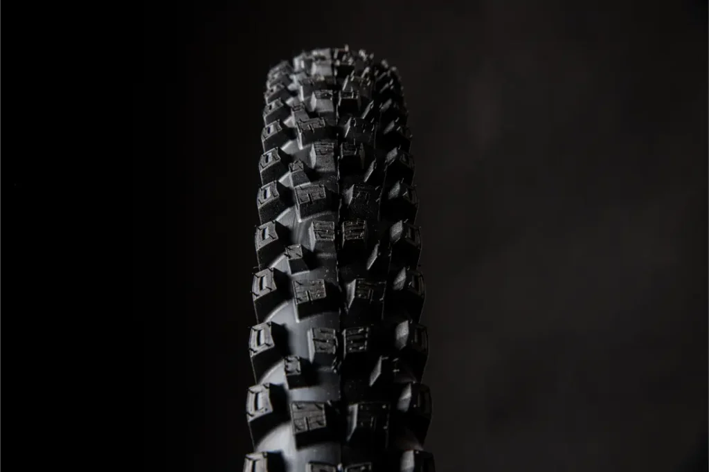 Primer plano de una rueda de bicicleta de montaña negra con relieve, como los neumáticos Pirelli Scorpion MTB, sobre un fondo oscuro y liso.