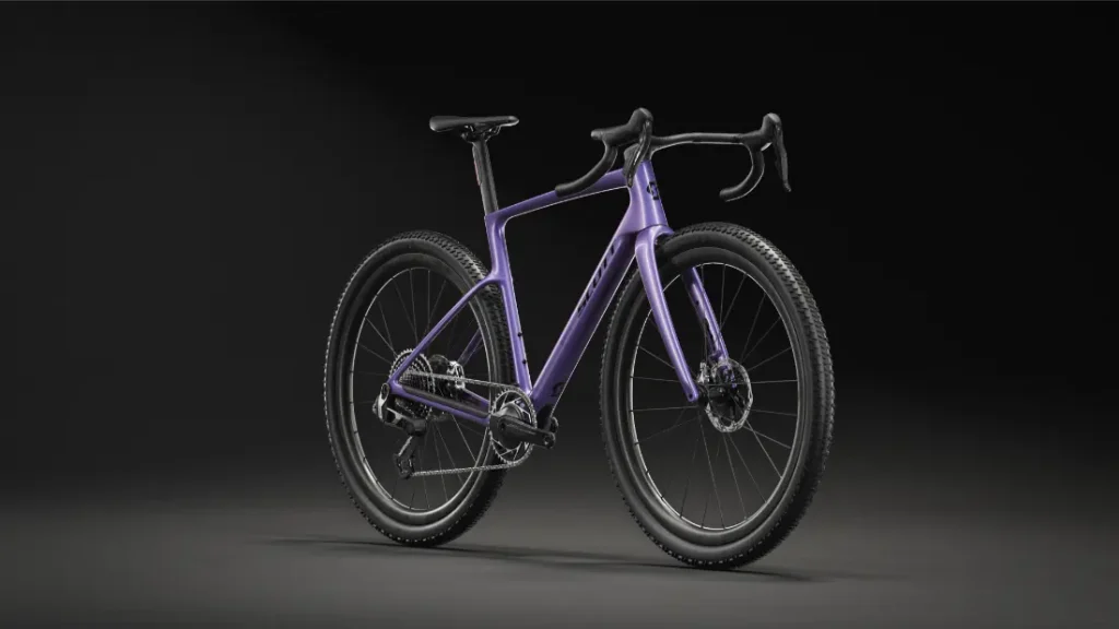 Se muestra una bicicleta polivalente SCOTT Addict Gravel 2027 en color morado, con manillar curvo y frenos de disco, sobre un fondo negro, ligeramente girada hacia la derecha. Perfecta para paseos cómodos por cualquier terreno.