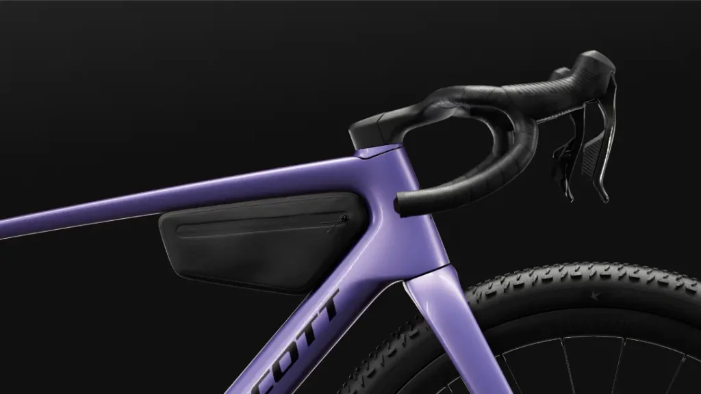 Primer plano de una bicicleta SCOTT Addict Gravel 2027 de color morado, con especial atención al manillar, el cuadro y una bolsa negra para accesorios fijada en el triángulo del cuadro, todo ello sobre un fondo negro, que refleja el espíritu polivalente de esta bicicleta gravel.