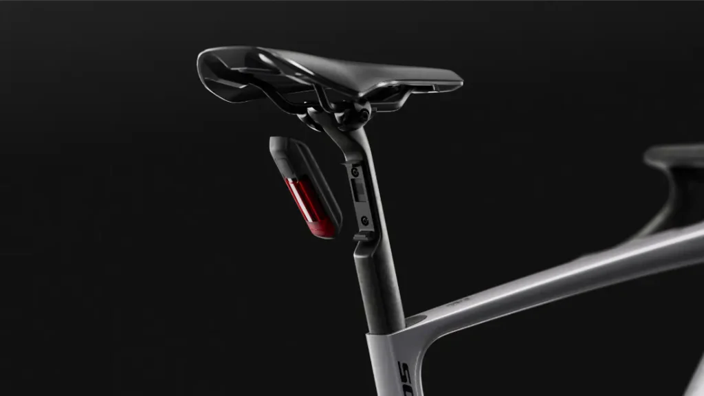 Primer plano del sillín, la tija del sillín y el cuadro de una bicicleta SCOTT Addict Gravel 2027, de colores negro y gris, en la que destaca una luz trasera roja montada debajo del sillín; esta bicicleta es conocida por su diseño polivalente y cómodo, y aparece sobre un fondo oscuro.