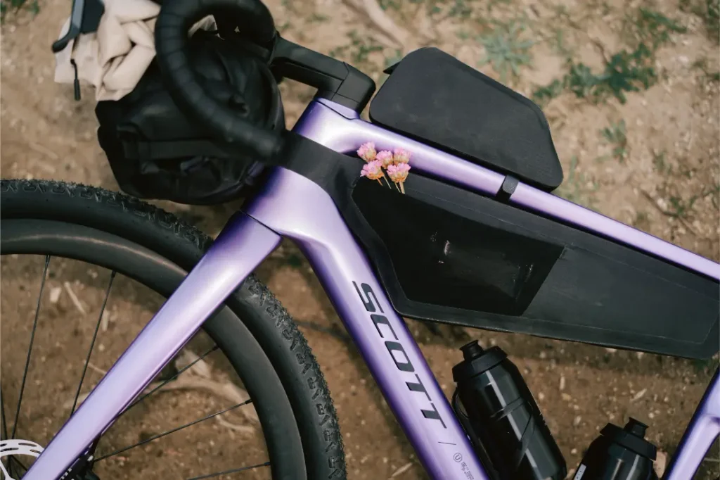 Un primer plano del cuadro morado de la bicicleta SCOTT Addict Gravel 2027 destaca su diseño polivalente, con dos bidones y unas pequeñas flores rosas metidas en la bolsa del tubo superior.