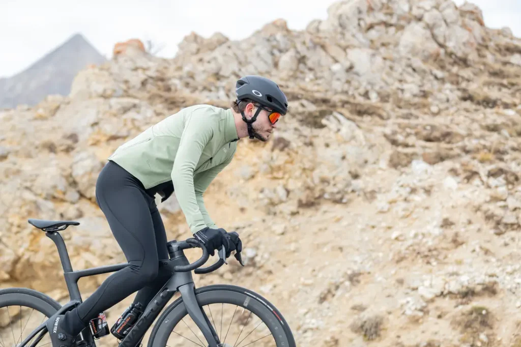 Un ciclista, que lleva casco y gafas de sol, sube en una bicicleta de carretera negra por un sendero rocoso al aire libre.