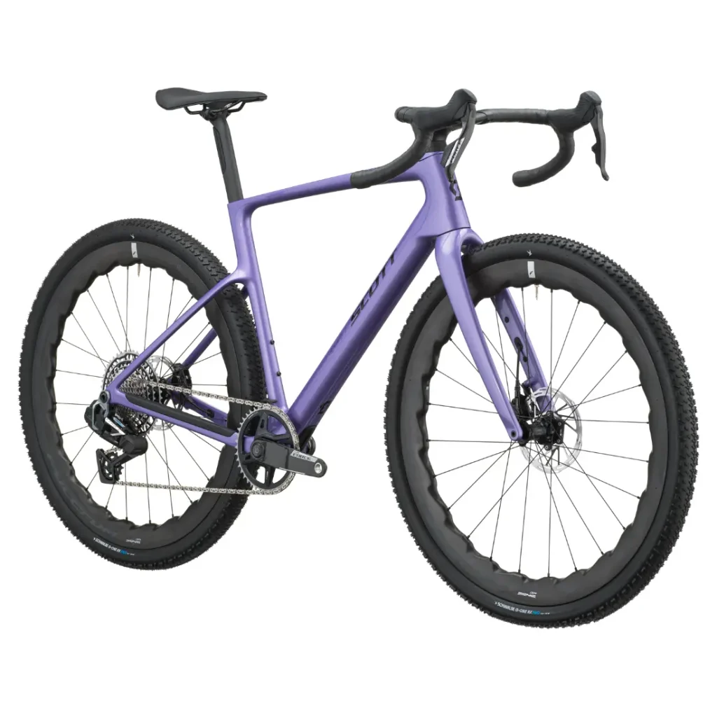 En un fondo blanco se muestra una bicicleta SCOTT Addict Gravel de color morado, con manillar de carretera, frenos de disco y neumáticos con tacos.