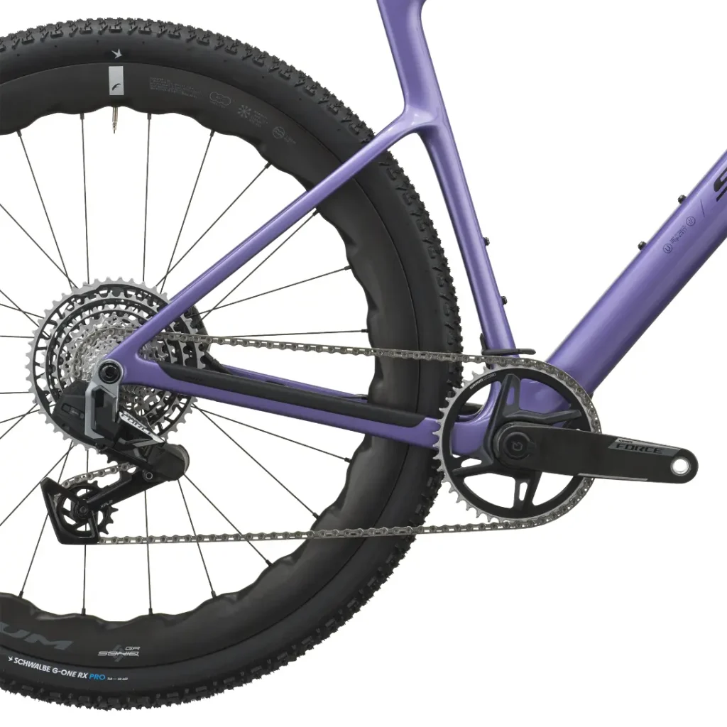 Primer plano de la rueda trasera, la cadena, el cassette, el desviador y la biela de una SCOTT Addict Gravel 2027 de color morado, en el que se aprecia parte del cuadro de la bicicleta y la banda de rodadura del neumático. El diseño versátil de esta bicicleta de gravel destaca sus prestaciones como bicicleta polivalente para diversos terrenos.