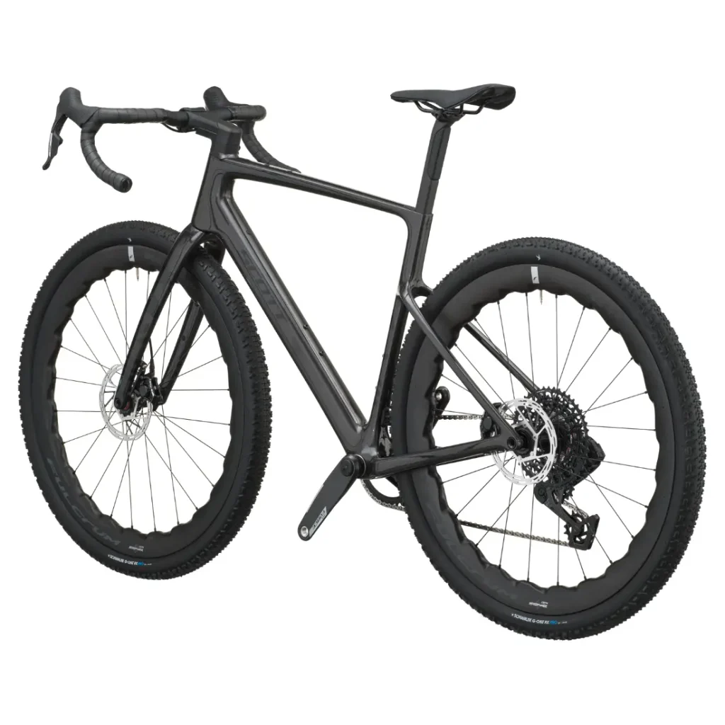 En un fondo blanco se muestra una bicicleta SCOTT Addict Gravel 2027 de color negro, con manillar de carretera, neumáticos de banda de rodadura gruesa, frenos de disco y cuadro de fibra de carbono. Este modelo polivalente ofrece una conducción cómoda en diversos terrenos.