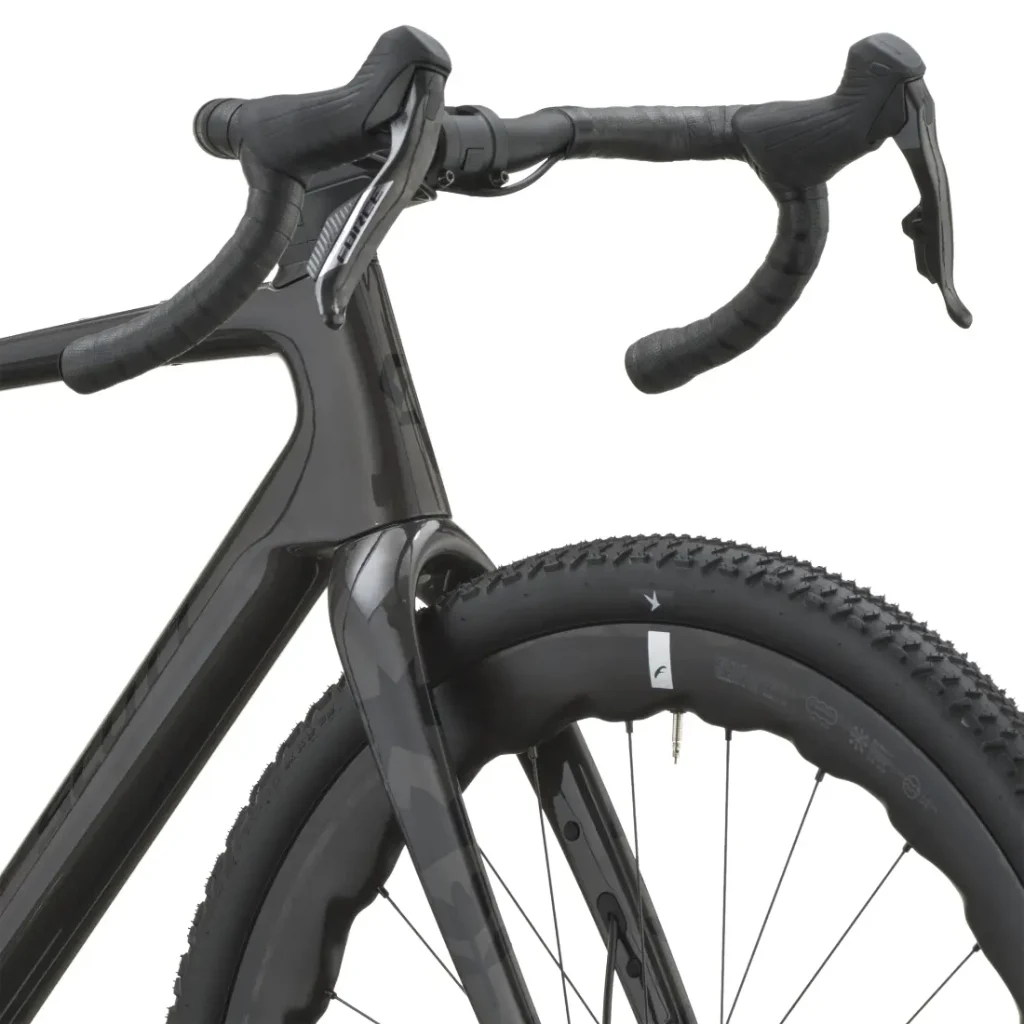 Primer plano de una bicicleta de carretera SCOTT Addict Gravel 2027 negra en el que se aprecian el manillar, las palancas de freno, la rueda delantera y parte del cuadro de carbono, con el dibujo de la banda de rodadura de la rueda visible. Esta bicicleta polivalente combina un diseño elegante con la comodidad para los ciclistas que buscan una bicicleta cómoda en cualquier terreno.