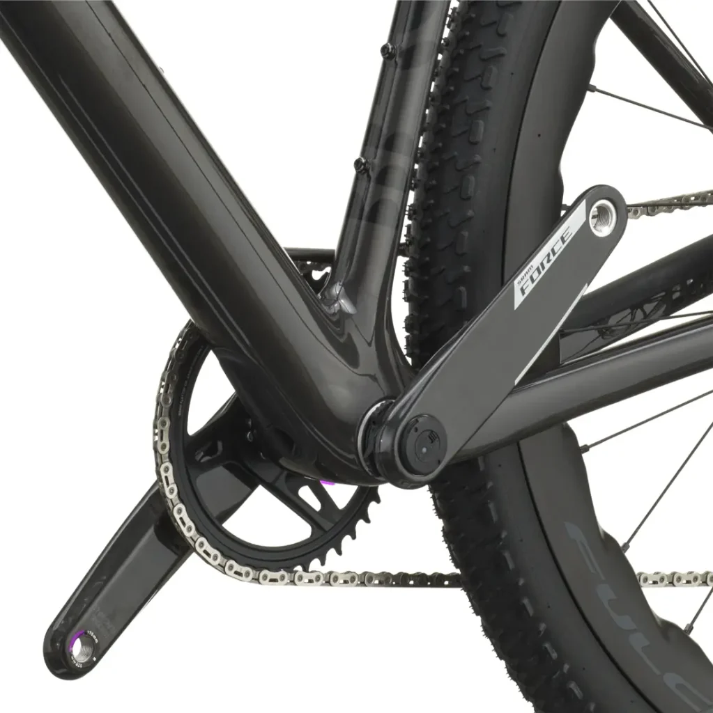 Primer plano de la transmisión de una bicicleta SCOTT Addict Gravel 2027 negra, en el que se aprecian el juego de bielas, el plato, la cadena y parte de la rueda trasera con un dibujo de banda de rodadura con tacos, lo que ilustra a la perfección el carácter polivalente de esta bicicleta de gravel.