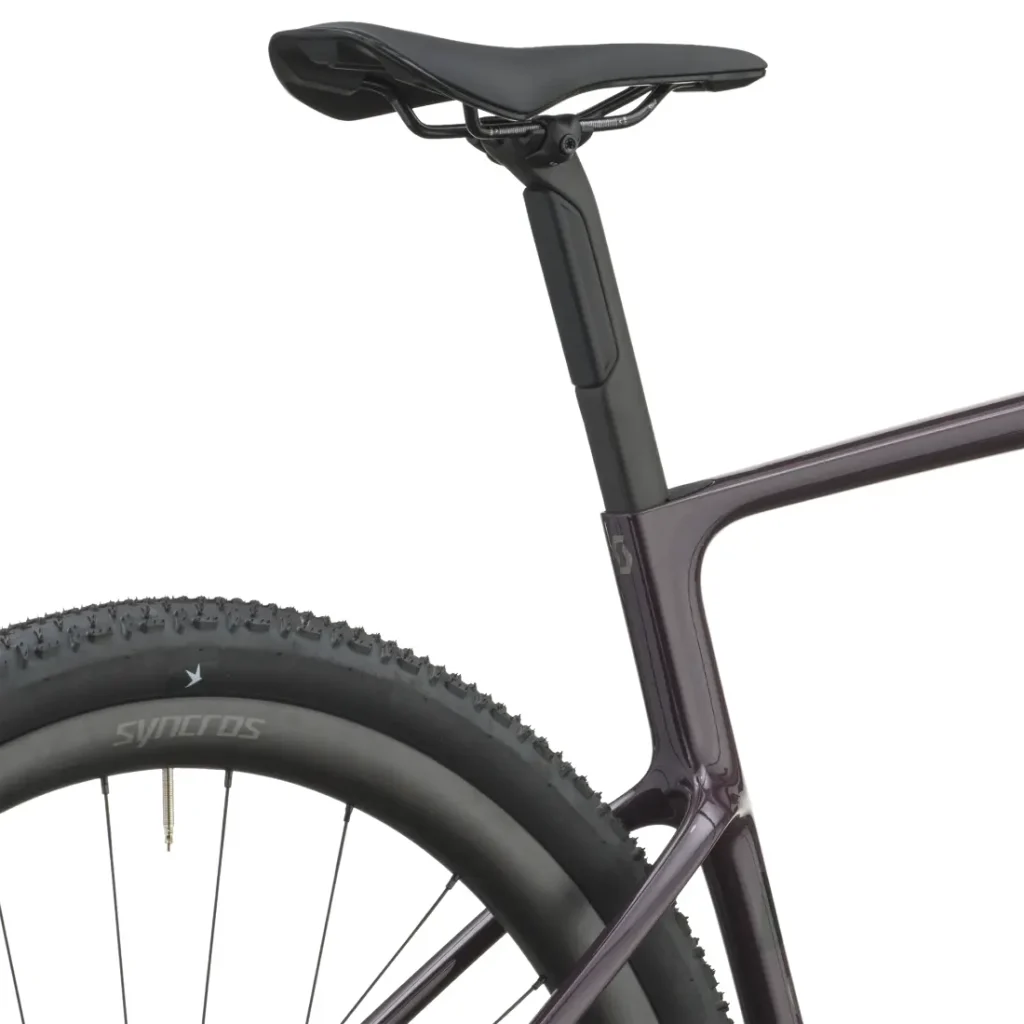 Primer plano de la parte trasera de una bicicleta, en el que se aprecian el sillín, la tija del sillín, parte del cuadro y la rueda trasera, con la banda de rodadura del neumático visible y el logotipo de Synchros en la llanta. El modelo SCOTT Addict Gravel 2027 aporta un toque de diseño moderno a esta configuración preparada para el gravel.