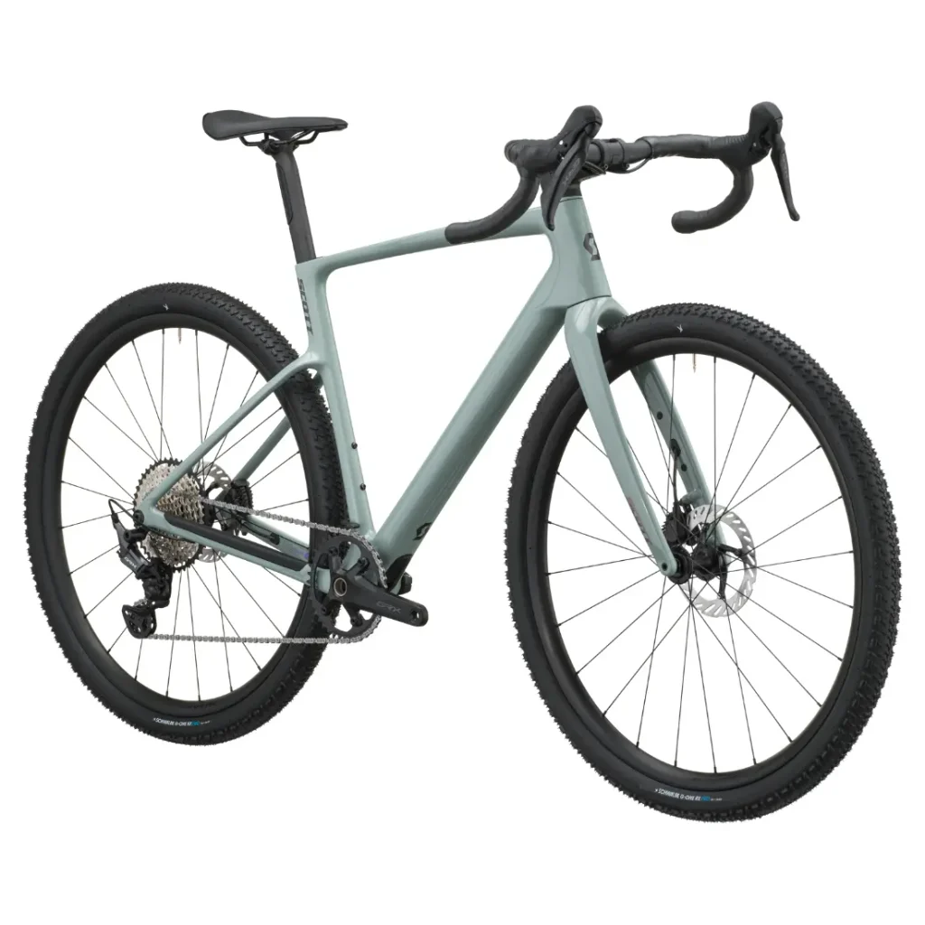 En un fondo blanco se muestra una bicicleta gravel SCOTT Addict Gravel 2027 de color verde claro, con manillar de carretera, frenos de disco y neumáticos con tacos, colocada en ángulo para resaltar su cuadro polivalente y su transmisión trasera.