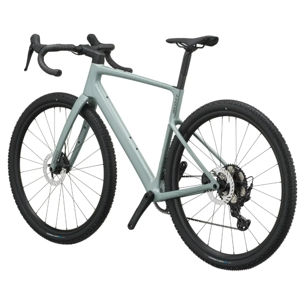 Bicicleta SCOTT Addict Gravel 2027 de color gris claro, con manillar de carretera, frenos de disco y neumáticos con tacos, vista desde un ángulo de tres cuartos trasero sobre un fondo blanco. Esta bicicleta de gravel, polivalente y cómoda, está diseñada para ofrecer versatilidad y comodidad en una gran variedad de terrenos.