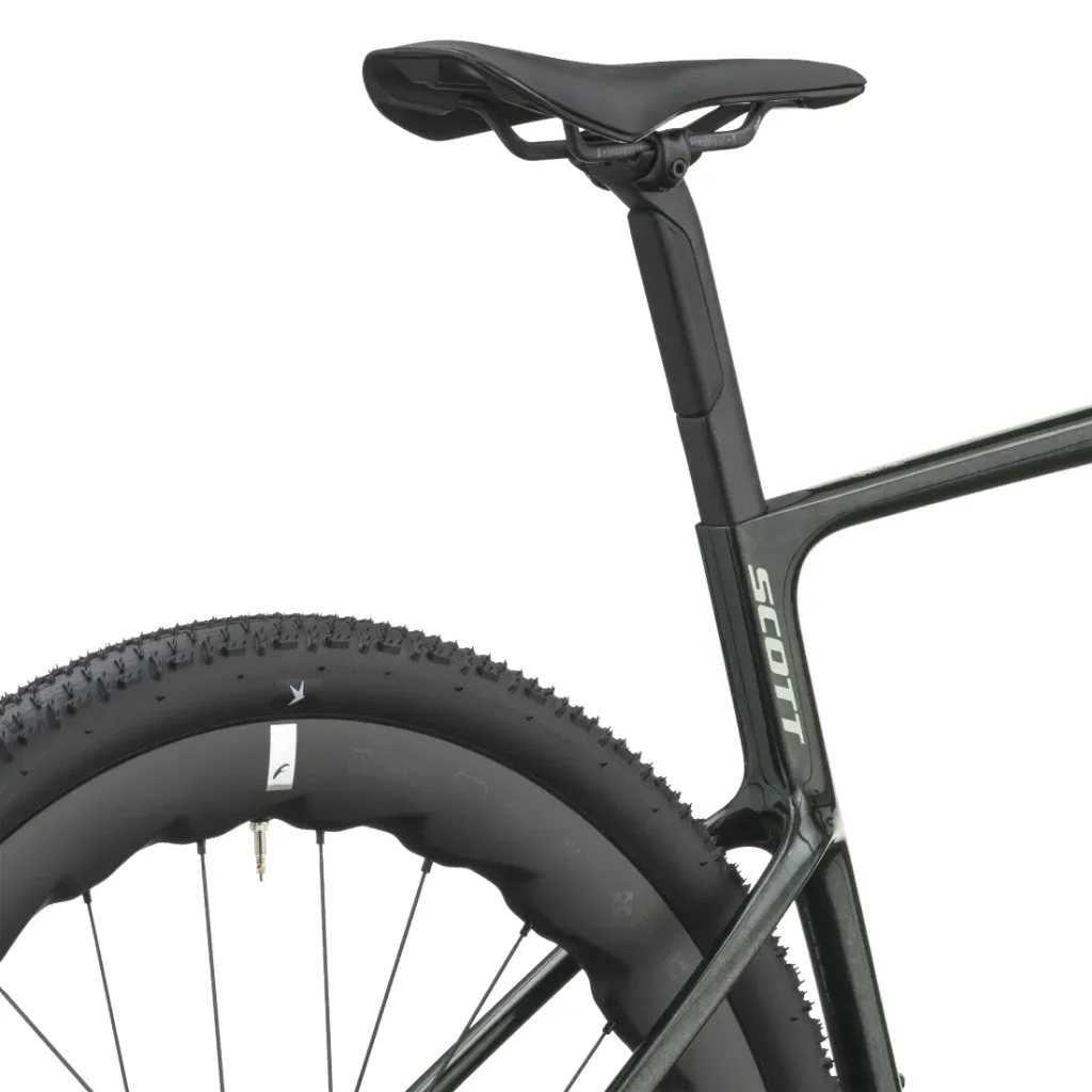 Primer plano de la rueda trasera, el tubo del sillín y el sillín de una bicicleta de gravel, en el que se aprecia una cubierta gruesa y parte del cuadro de la bicicleta con la inscripción «SCOTT Addict Gravel 2027». Este diseño polivalente destaca tanto por su resistencia como por su versatilidad para diferentes tipos de terreno.