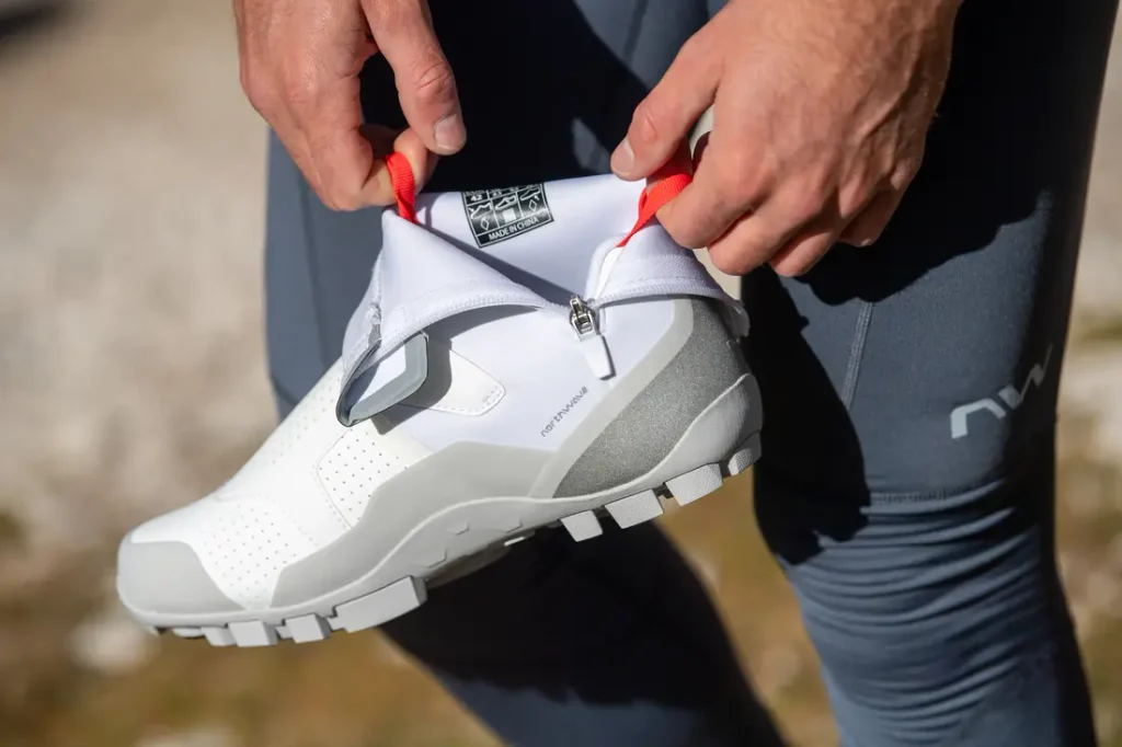Primer plano de una persona que se ajusta la cremallera de unas zapatillas deportivas blancas y grises mientras lleva unos leggings grises al aire libre.