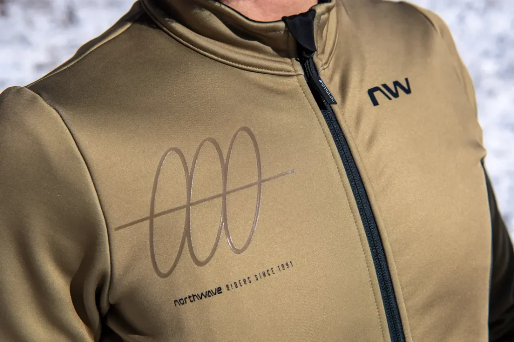 Una persona que lleva una chaqueta Northwave de color verde oliva con cremallera negra y un logotipo estampado en el pecho.